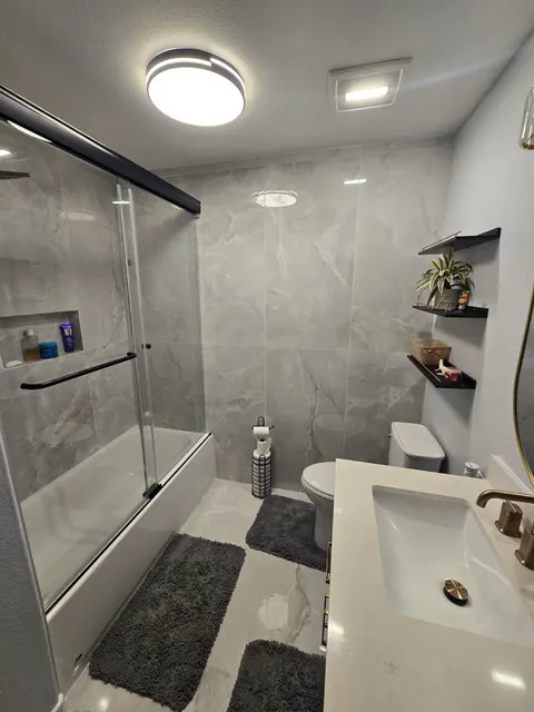 Wide bathroom view showing the completed black-header sliding tub enclosure