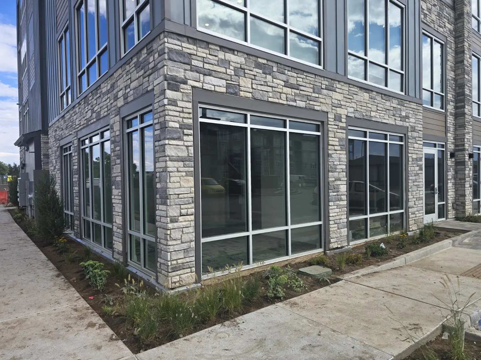 Corner storefront glazing wrapping two elevations of a stone-clad commercial suite in Thornton