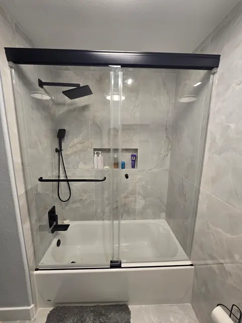 Abricos Glass completed sliding glass tub enclosure with a black header installed above a bathtub