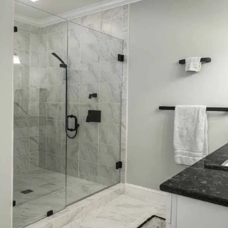 Agalite Estate hinged glass shower door and fixed panel with black hardware in a marble-tiled shower