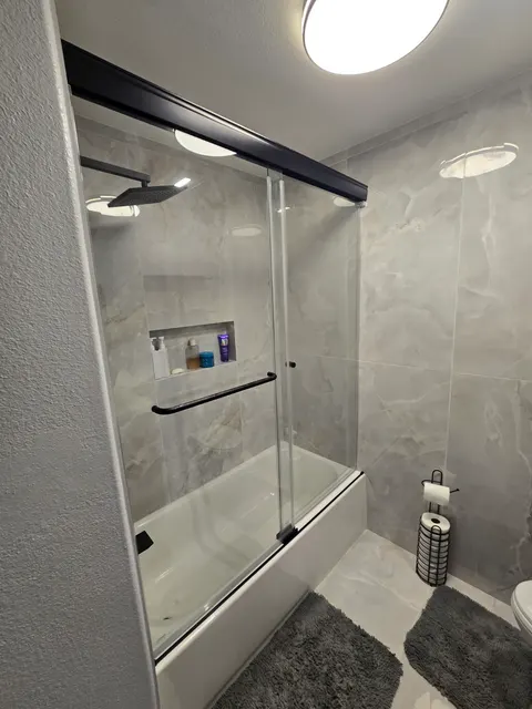 Angled view of the completed sliding glass tub enclosure and black hardware