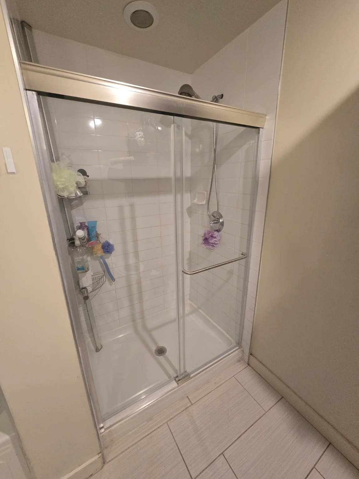 Installed sliding glass shower enclosure with a silver-tone frame and handle