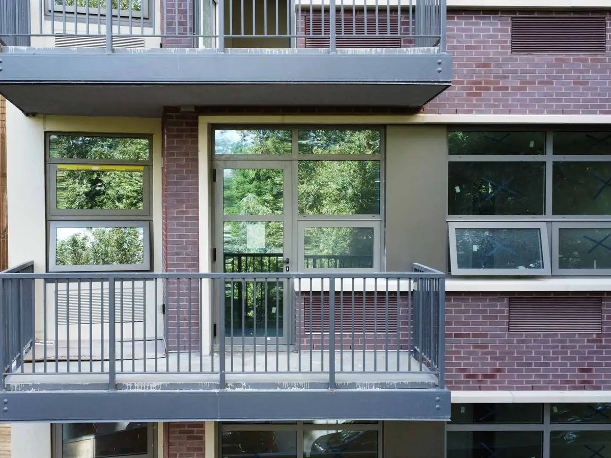 Balcony framed by large sliding glazed panels running in aluminum tracks behind a metal railing.