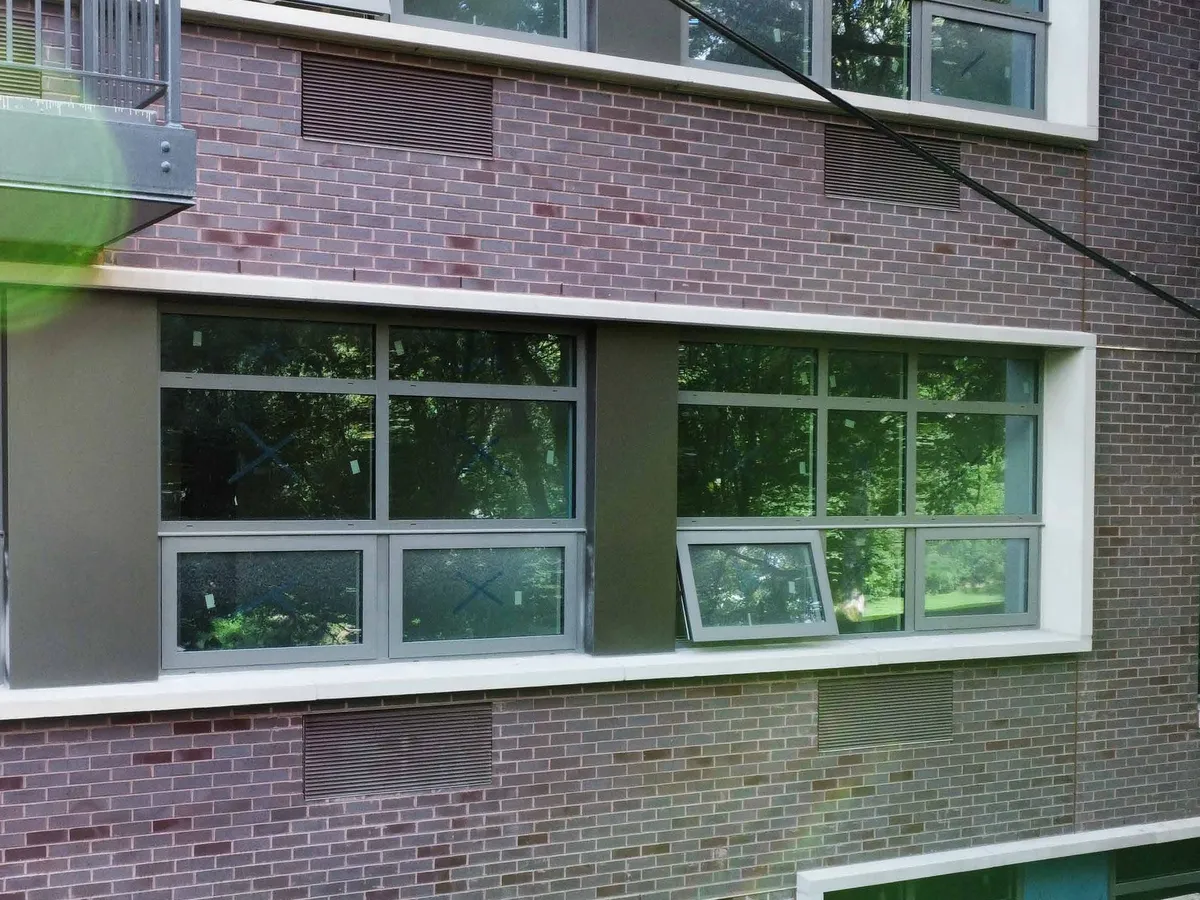 Building elevation with an aluminum window sash tilted open at the top for ventilation.
